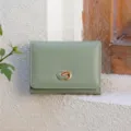 Close-up detail of a minimalist light green trifold women wallet with chic metal clasp on texture. - Light Green