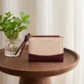Detail view of a short bi-fold women wallet with zipper, wristlet knot, and fabric texture. - Wine Red