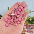 Close-up of sparkling pink round resin rhinestones in hand, perfect for DIY craft and art decor. - Round Faceted Plated Bottom (12mm) / 100 Pieces/Pack / Peach Red
