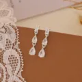 Primo piano dettagliato di orecchini pendenti in zircone scintillante con finitura argento. - Nappa a Tre Pietre / Argento