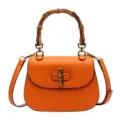 Sac de selle rétro en cuir orange avec poignée en bambou naturel et élégante fermeture. - Orange