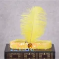 Detail shot of a 1920s vintage yellow sequin feather headband with a large amber gem decoration. - Yellow