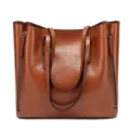 Close-up detail of the brown oil leather tote handbag, showing texture and side zipper design. - Brown