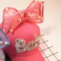 Close-up of kids pink baseball cap with large lace bow, pearls and rhinestone Baby text. - Watermelon red