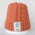 Gros plan détaillé du bonnet en tricot torsadé orange avec écusson textuel blanc. - Taille unique / Orange