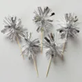 Close-up detail of silver tinsel cake toppers, sparkling metallic fringe firework picks for desserts. - Silver