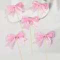 Close-up detail of pink double-layer bow cake toppers on wooden sticks for party decor. - Pink