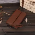 Primer plano detallado de un bolso de mano marrón para hombre con correa suave en madera. - Café