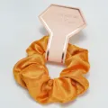 Detailed close-up of a golden satin hair scrunchie with a Tie the Knot bridesmaid card - Orange