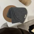 Dunkelgrauer Strickschal Detail mit Rippenmuster und Stoffetikett auf weißem Tisch. - Dunkelgrau