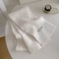 Detaillierte Ansicht eines kuscheligen, weißen Strickschals, ordentlich gefaltet auf dem Tisch. - Creme