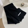 Schwarzer Strickschal Detail mit Rippenmuster und weißem Etikett auf weißem Tisch. - Schwarz