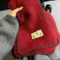 Detailed shot of a red knitted woolen scarf with dark trim and a cute cat label texture. - Burgundy