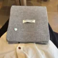 Grey wool blend knitted scarf with decorative shell charm and handmade label variant detail. - Light Gray