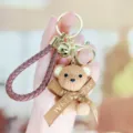 Leuke hars geweven textuur teddybeer sleutelhanger met gevlochten riem en strik voor tas. - Zittende harsbeer met vlinderdas - koffiekleur