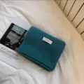 Primer plano de bufanda de punto verde oscuro, doblada ordenadamente sobre ropa de cama blanca. - Azul Óleo
