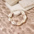 Dettaglio di un braccialetto di conchiglie in stile spiaggia su sfondo di sabbia al sole. - Bracciale