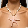 Nahaufnahme der Halskette mit rosa Seestern-Anhänger und weißen Perlen am Modell. - Rosa