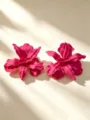 Close-up detail van opvallende magenta bloem oorbellen met metallic bloembladtextuur. - Roze