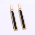 Close up of geometric long gold metal dangle earrings with elegant black inner design. - Gold + Black