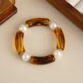 Dettaglio di un bracciale elastico in resina ambrata e perle con accenti dorati. - Marrone