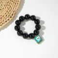Gros plan sur bracelet d'Halloween en perles noires brillantes avec un pendentif crâne. - Style Tête de Mort / 5.5cm Diamètre Intérieur / Noir (S-001)