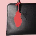 Close up detail of a black leather handbag featuring a red country map pendant accessory. - Red