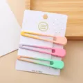 Gros plan de trois pinces à cheveux bec de canard en métal dégradé coloré sur carte. - Gouttes d'eau ajourées (Ensemble de 3 pièces couleurs bonbon)