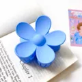 Gros plan détaillé d'une pince à cheveux fleurie bleue mate sur un livre ouvert. - Grande pince à cheveux fleur bleu lac