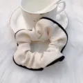 Gedetailleerde opname van een elegante off-white stoffen haarscrunchie met zwarte rand. - Crèmewitte omrande accessoires
