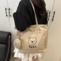 Detail shot of the beige canvas tote bag showing the cute bear print design and front pocket. - Khaki