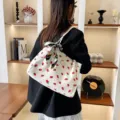 Detailed view of white corduroy tote bag with red strawberry print and chic scarf decoration. - White Strawberry