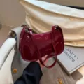 Detail view of the elegant dark red patent leather shoulder bag with fine strap and zip closure. - Red