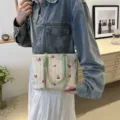 Woven straw tote bag with cute cherry embroidery and green handles, detail view on model. - Green