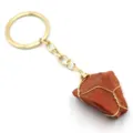 Dettaglio pendente in pietra di cristallo rosso grezzo, primo piano anello portachiavi e catena dorati. - Pietra rossa avvolta in filo dorato