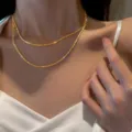 Primer plano detallado del collar de cadena brillante de doble capa usado en el cuello. - Dorado