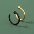 Close-up van U-vormige neppe neusringen in zwart en goud met strak open ontwerp. - Zwart En Goud