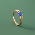 Vista dettagliata di un anello aperto dorato con pietra di zirconia blu e gambo sdoppiato. - Stile Blu Tondo Fascia Divisa (SE1502)