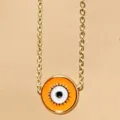 Goldfarbene Kette mit orangefarbenem runden Anhänger mit bösem Blick Motiv als modischer Schmuck. - Orange