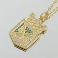Collar con colgante de escudo chapado en oro con piedras preciosas blancas y verdes - Insignia Dorada