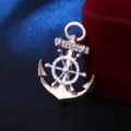 Detaillierte Nahaufnahme einer stilvollen Anker- und Schiffslenker-Brosche mit klaren Kristallen. - Goldener Anker & silbernes Steuerrad