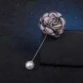Gros plan d'une broche camélia en tissu gris avec longue épingle perlée sur un support noir. - Gris