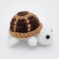 Detail einer handgefertigten Häkelschildkröte mit braun gemustertem Panzer und weißem Körper. - 8.5cm / Puppen-Stil / Braun