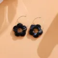 Nahaufnahme von schwarzen Acryl Blumen Ohrringen mit goldenen Reifchen, süßer Modeschmuck. - Blumen-Ohrringe Paar / Schwarz