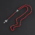 Detalle de primer plano del collar de rosario con cuentas rojas y elegante cruz plateada. - Rojo