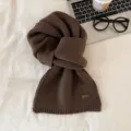 Vista detallada de bufanda de punto marron con textura suave y pequena etiqueta de cuero. - 1 Marrón café