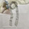 Détail d'un foulard en soie long et étroit à pois noirs et blancs, accessorio élégant. - Beige à Pois