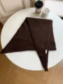 Close-up view of a cozy dark brown wool-blend triangular scarf neatly arranged on a white table. - Coffee
