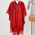 Detail view of a stylish red knitted hooded poncho with fringe and colorful accents. - Red