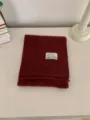 Detail shot of a dark red knitted winter scarf, neatly folded with a small brand label. - Burgundy